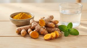 Racines et poudre de curcuma à côté d'un verre d'eau et de feuilles de menthe sur une table en bois.