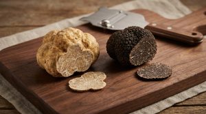 Une truffe blanche et une truffe noire coupées sur une planche en bois avec une mandoline à truffe en arrière-plan.